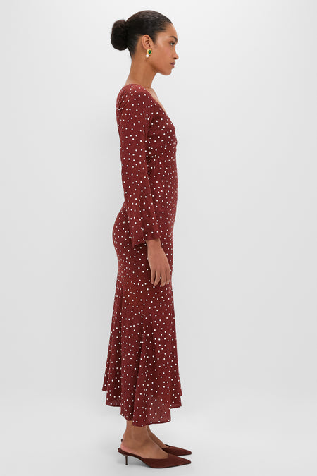 Side-profile of a woman in the Burnt Umber Narah Maxi Dress, featuring playful polka dots, long sleeves, and a flared hem for an effortless, high-end style.