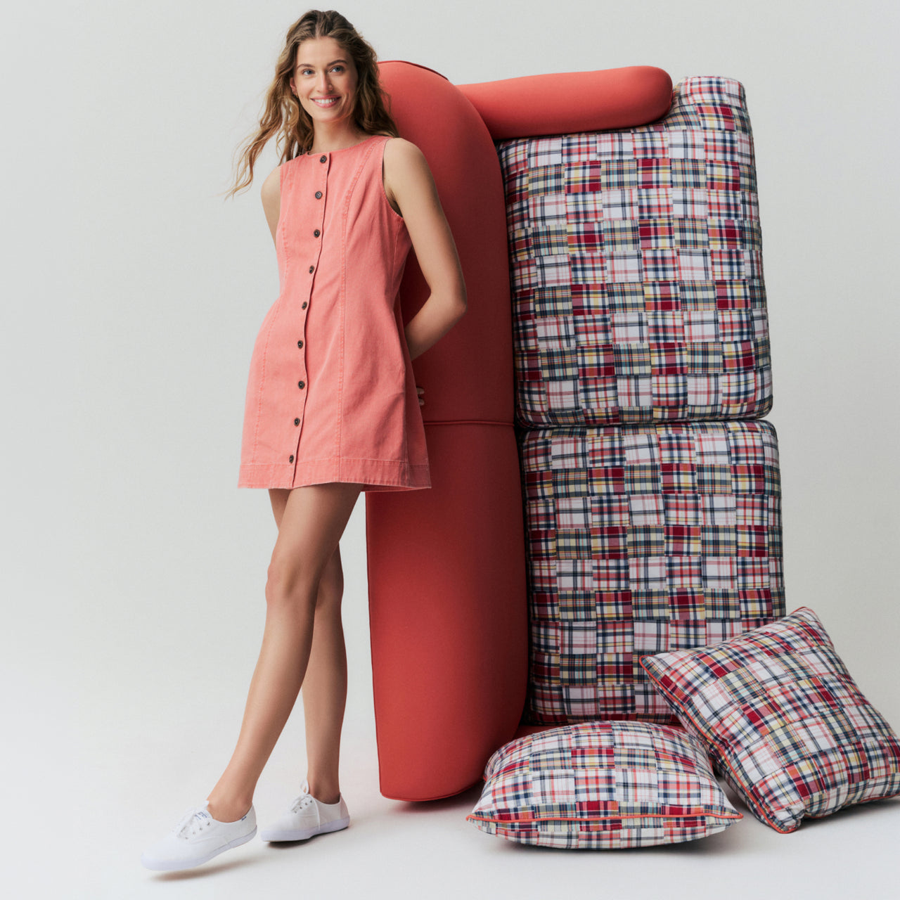 Woman in a red mini dress leaning on a couch that's been turned onto it's side. 
