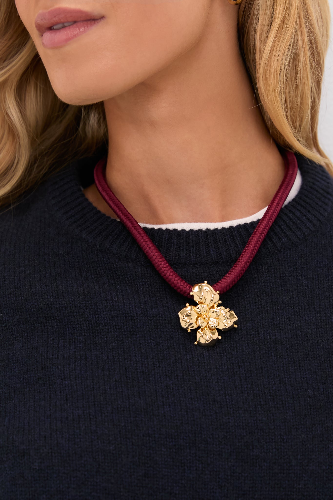Close-up of the Maroon Lelani Necklace on a woman, featuring a burgundy cord and detachable gold flower pendant, epitomizing classic, effortless style with high-end, fun versatility.