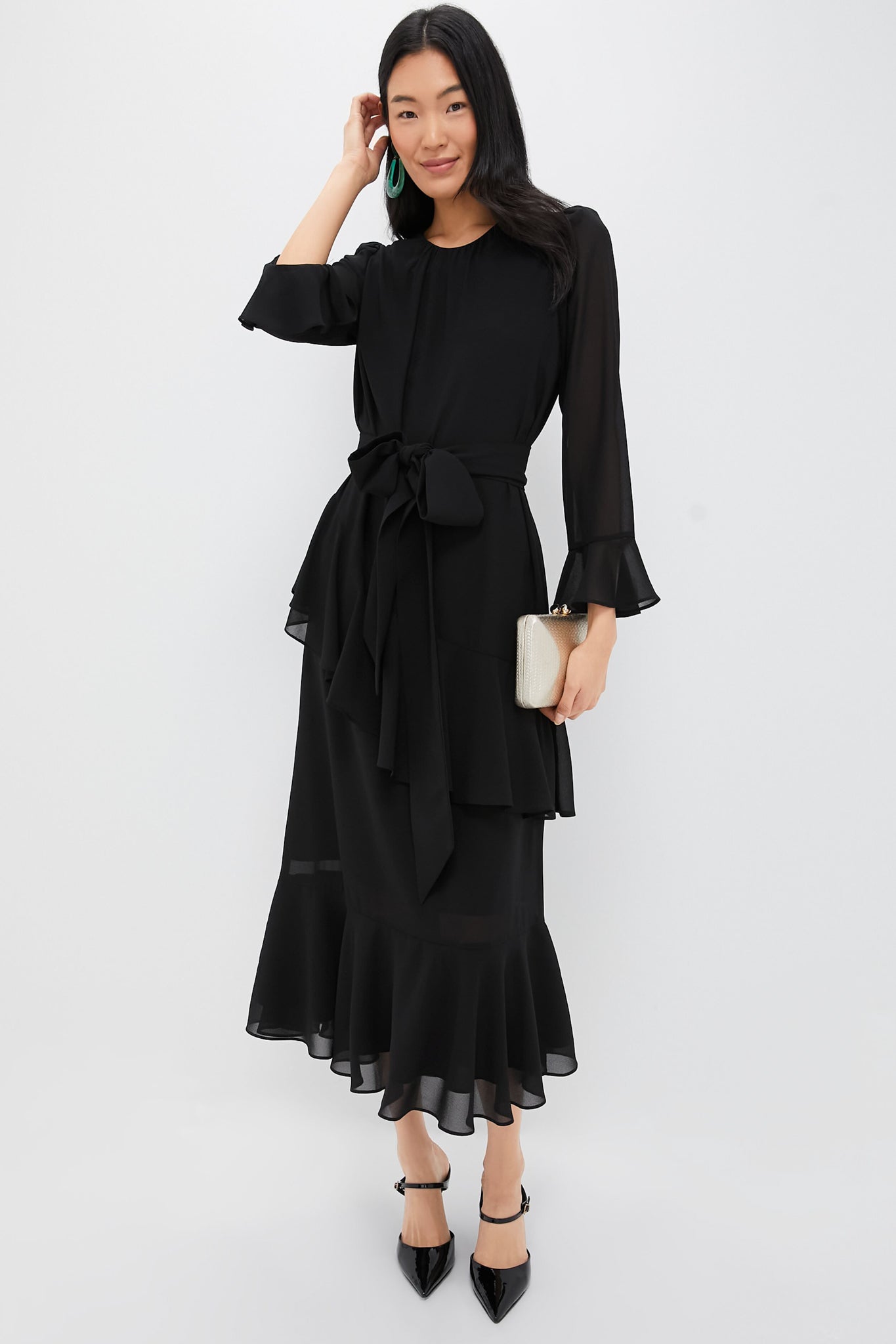 Model in a classic Black Chiffon Sasha Dress with ruffled sleeves, self-tie belt, and flounced hem, accessorized with statement earrings and clutch, epitomizing effortless high-end style.