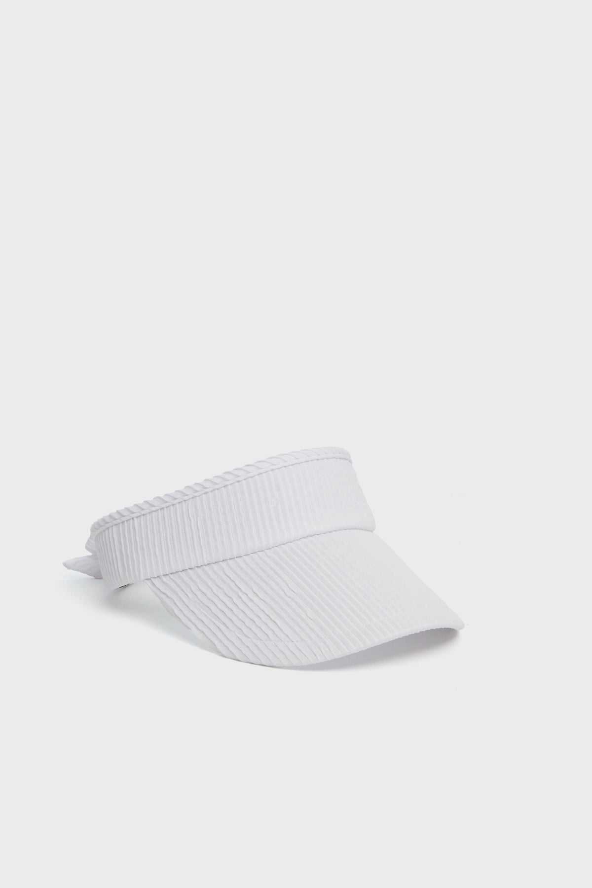A sleek Lele Sadoughi white ribbed visor cap, crafted from a ruched poly blend for comfort and style, featuring an adjustable back strap.