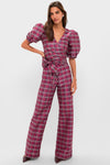 A woman wearing a Louise Berry Tartan pink plaid jumpsuit with puffed short sleeves, wide-leg silhouette, and tie belt stands against a plain light background.