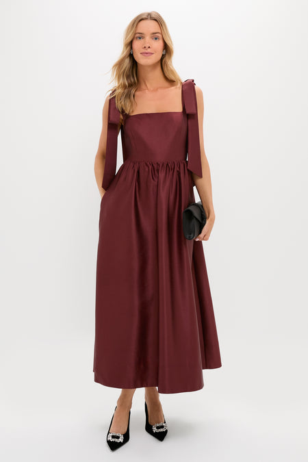 Woman in an Oxblood Dupioni Bow Esme Dress, exuding classic elegance with a square neckline and full skirt. Effortlessly styled with black clutch and heels.