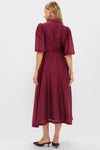 Woman in a classic, effortless Oxblood Cindy Midi Dress with puff sleeves and waist tie, embodying high-end, fun style.