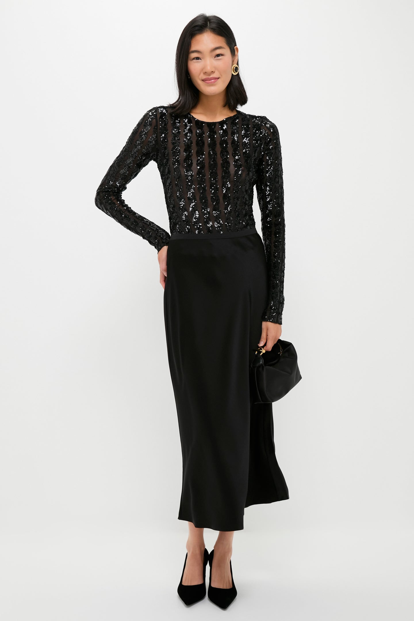 A woman poses against a plain background in a Polo Ralph Lauren long-sleeved black sequined top and black double-faced satin split skirt, holding a small black handbag and wearing black heels—perfect for cocktail parties.
