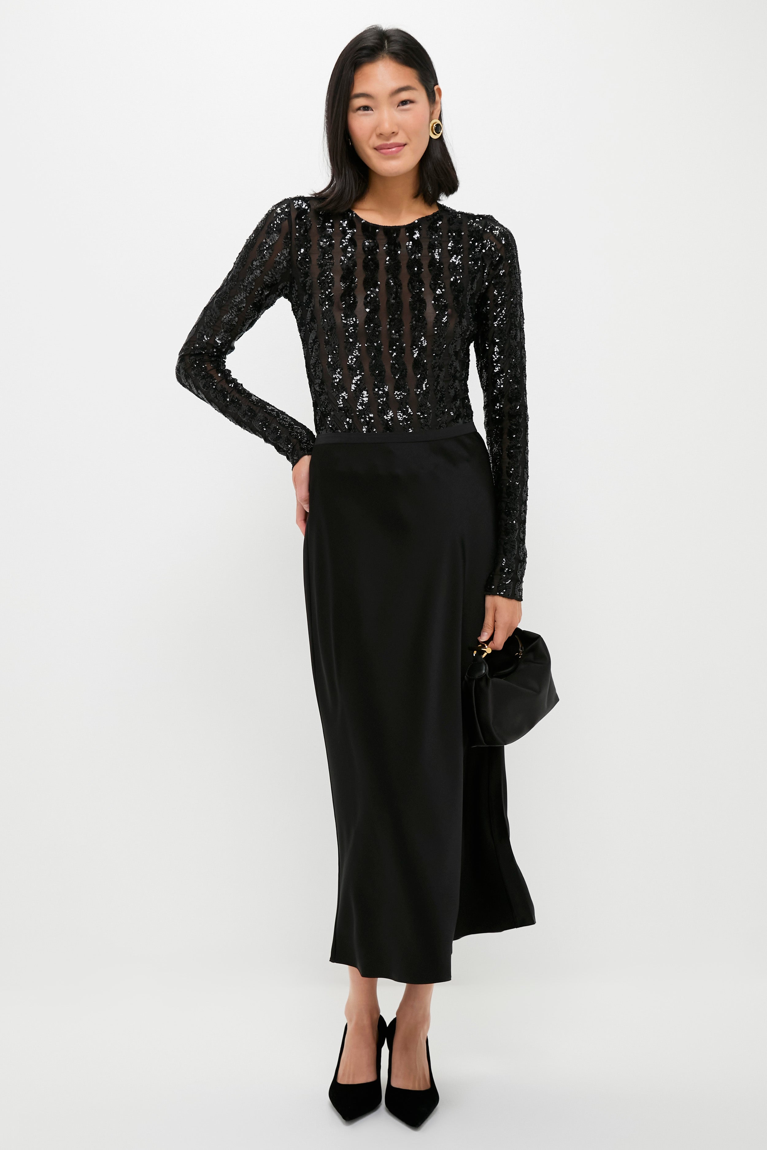 A woman poses against a plain background in a Polo Ralph Lauren long-sleeved black sequined top and black double-faced satin split skirt, holding a small black handbag and wearing black heels—perfect for cocktail parties.