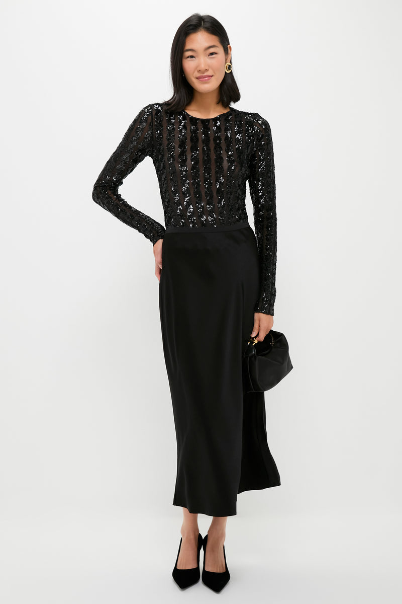 A woman poses against a plain background in a Polo Ralph Lauren long-sleeved black sequined top and black double-faced satin split skirt, holding a small black handbag and wearing black heels—perfect for cocktail parties.