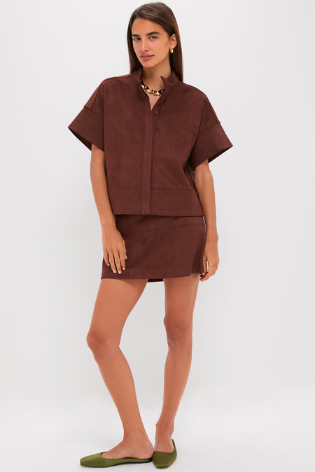 Woman models the Ganache Vegan Suede Meg Mini Skirt, embodying effortless style with a classic A-line silhouette, paired with a matching chocolate brown shirt and gold accessories.