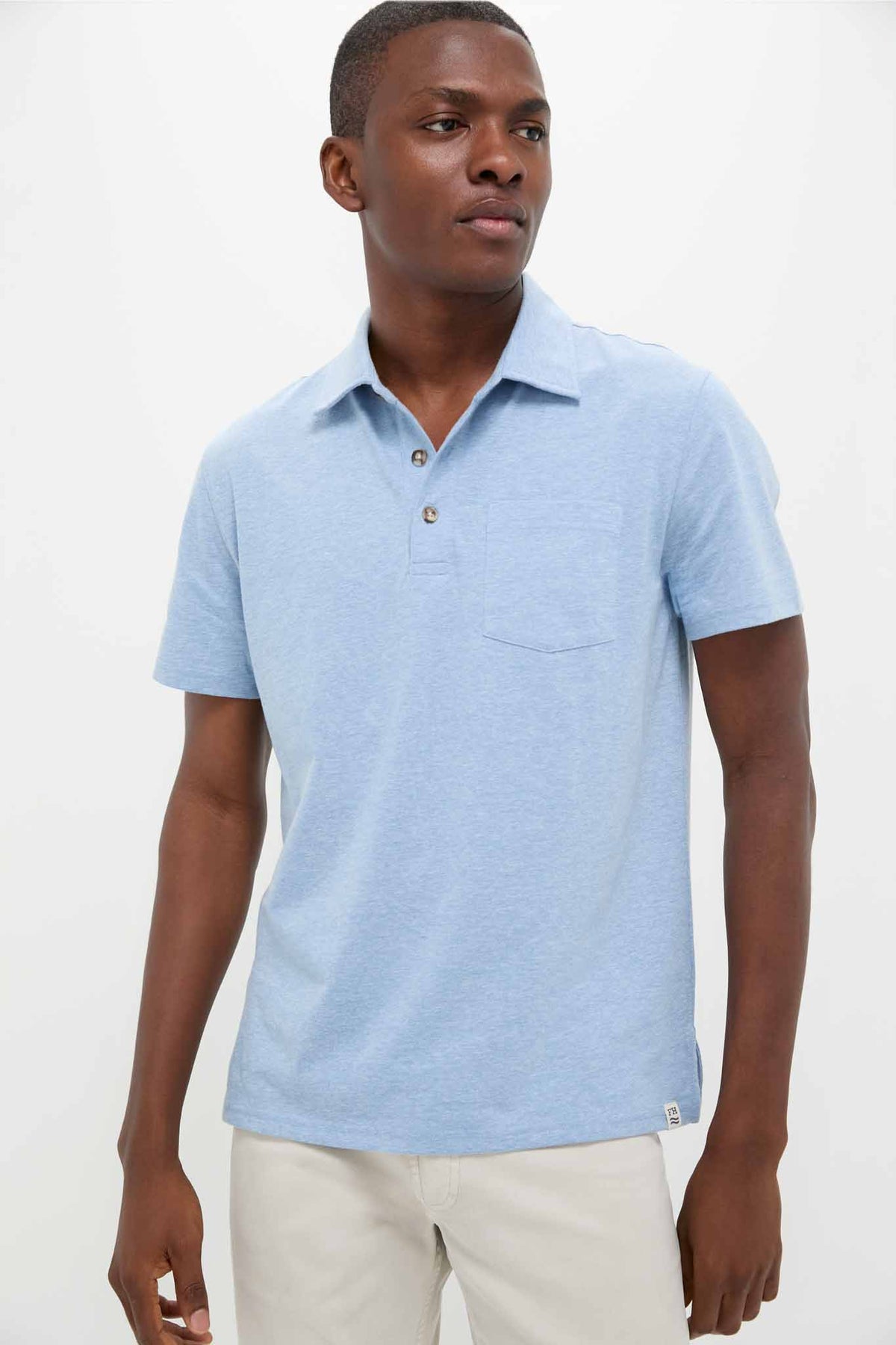 A man stands confidently, showcasing sustainable fashion in a Fair Harbor light blue short-sleeve organic cotton polo and light-colored pants.