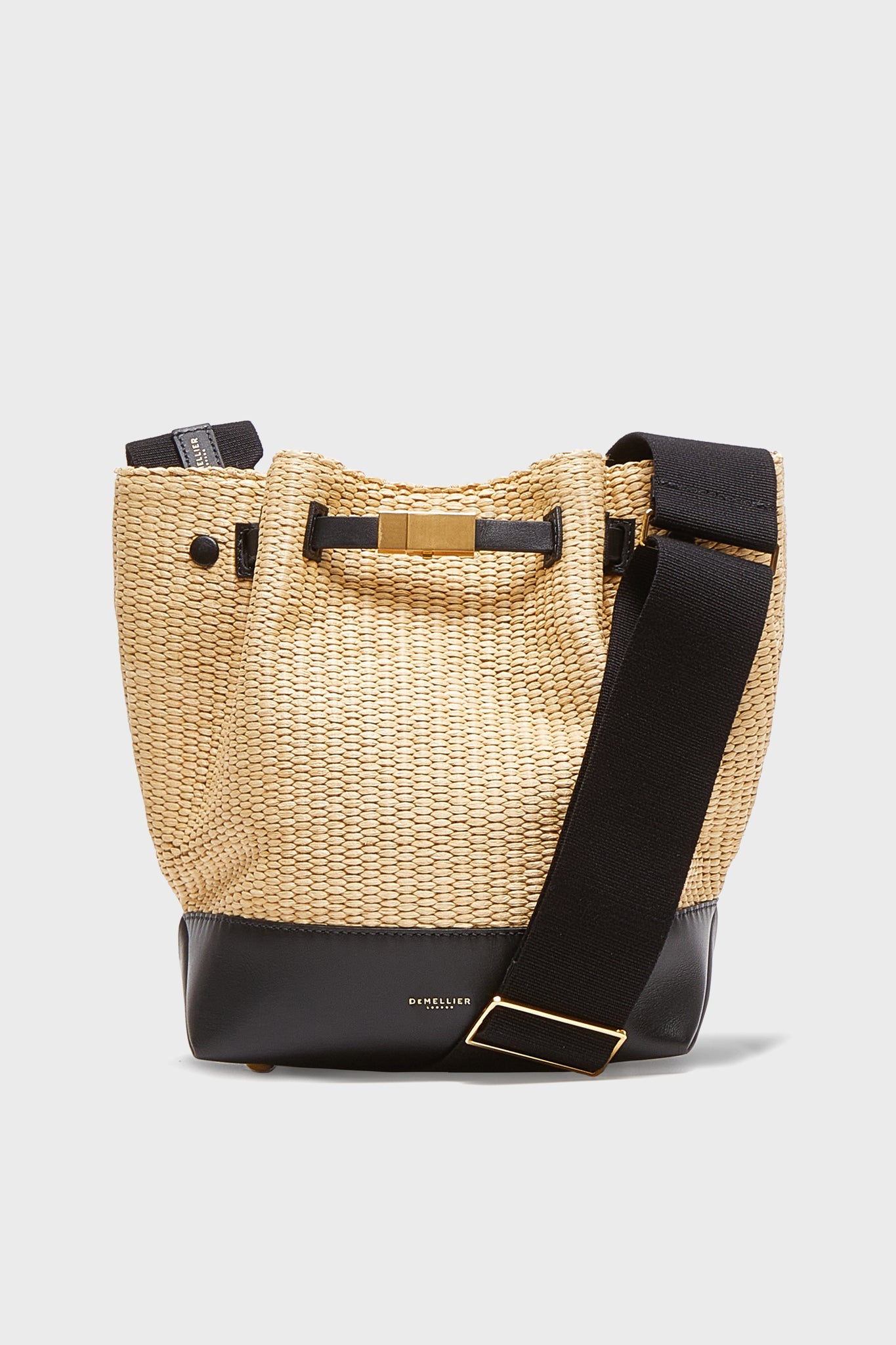 Demellier’s woven raffia bucket bag features a black leather base, wide black shoulder strap, and gold buckle for a chic crossbody upgrade.