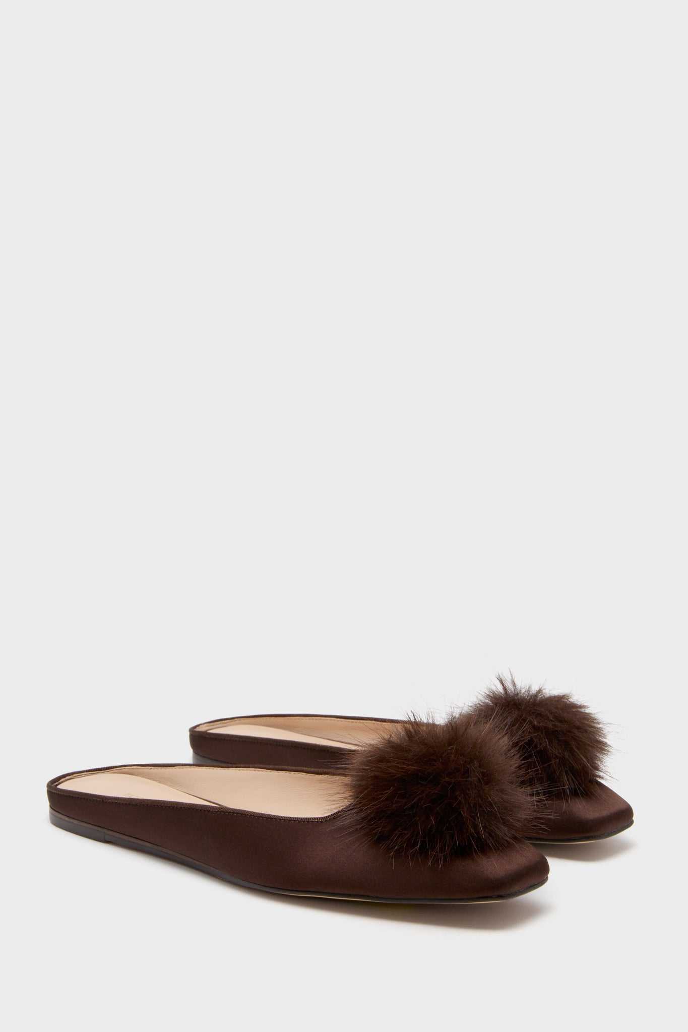 A pair of Tuckernuck Shoes brown satin mule flats with fluffy pom-pom detail on the toes, displayed against a plain background.