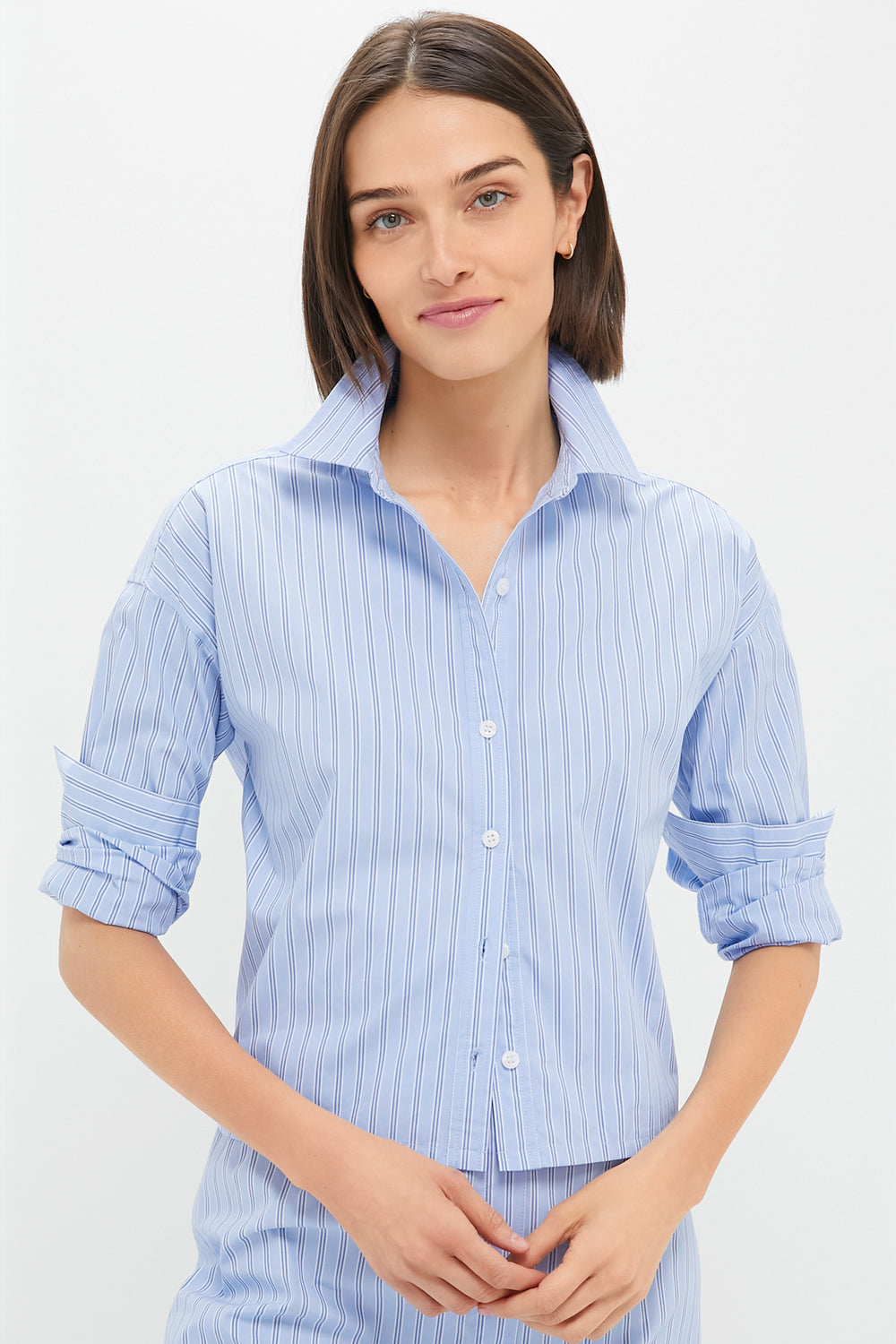 A woman wearing a Tuckernuck blue and white thin stripe button-down shirt with rolled-up sleeves.