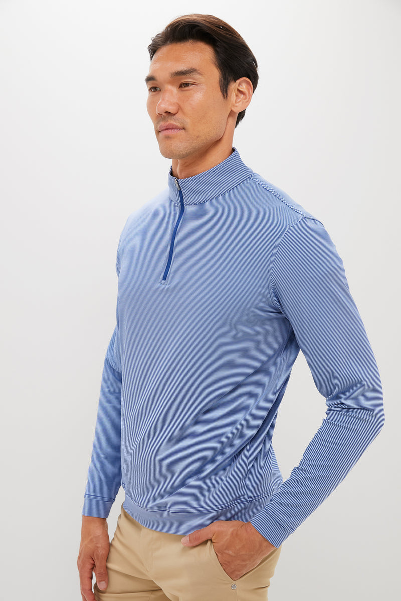 A man in a light blue Peter Millar quarter-zip performance pullover and beige pants stands against a plain, light-colored background.