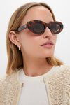 Person wearing Tortoise Roma Sunglasses with chic oval frames and dark lenses, exuding an effortless, high-end style paired with a curly-fleece jacket and elegant earrings.