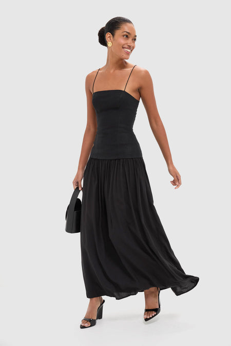 Smiling woman in a classic Black Lenise Maxi Dress with a fitted bodice, flowing skirt, sleek bun, and gold earrings, exuding effortless, high-end style.