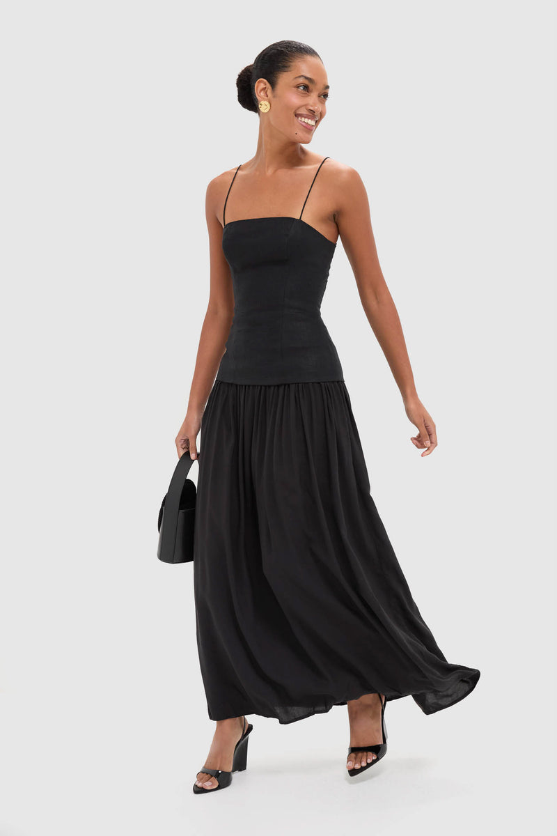 Smiling woman in a classic Black Lenise Maxi Dress with a fitted bodice, flowing skirt, sleek bun, and gold earrings, exuding effortless, high-end style.