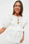 A woman smiles brightly wearing the Moon River White Ruffle Eyelet Top, featuring puff sleeves, a lace-up front, and eyelet detailing.