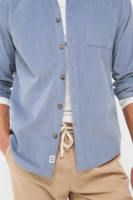 Classic Maritime Wilder Stretch Corduroy Shirt in light-blue, unbuttoned over a white T-shirt, paired with camel-tan drawstring trousers. Effortless, high-end style for versatile, fun moments.