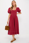 A woman in a Moon River red puff sleeve midi dress and brown flats, carrying a brown square handbag, showcases a vintage-inspired look.