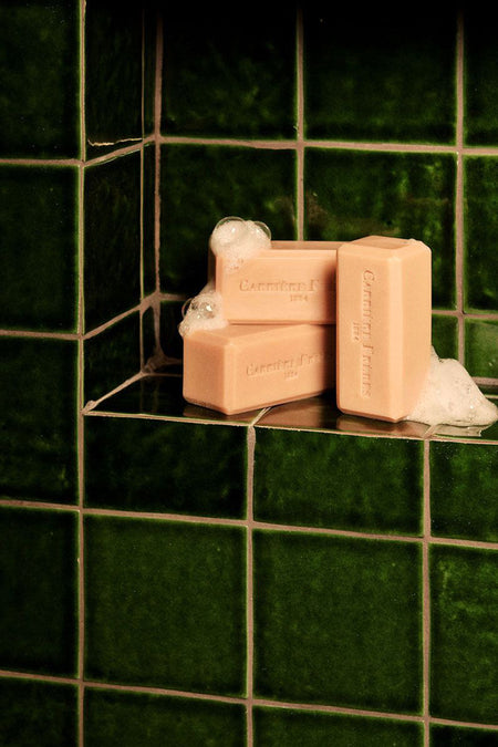Florae Solid Body Soap in a classic, deep-green tiled niche displays an effortless and fun arrangement of peach bars, exuding a high-end floral scent.