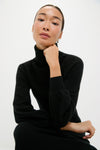 Young woman in a classic Black Cashmere Turtleneck Maxi Dress, showcasing its effortless elegance with blouson sleeves and ribbed finishes for a high-end, versatile look.