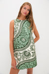 A woman stands with poise wearing a Tuckernuck sleeveless mod mini dress, featuring a green and white floral pattern.