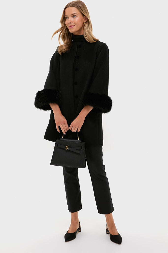 A woman wears a Tuckernuck Black Wool Fur Cuff Coat with fur-trimmed sleeves, paired with black pants, heels, and a black handbag, standing against a plain light background.