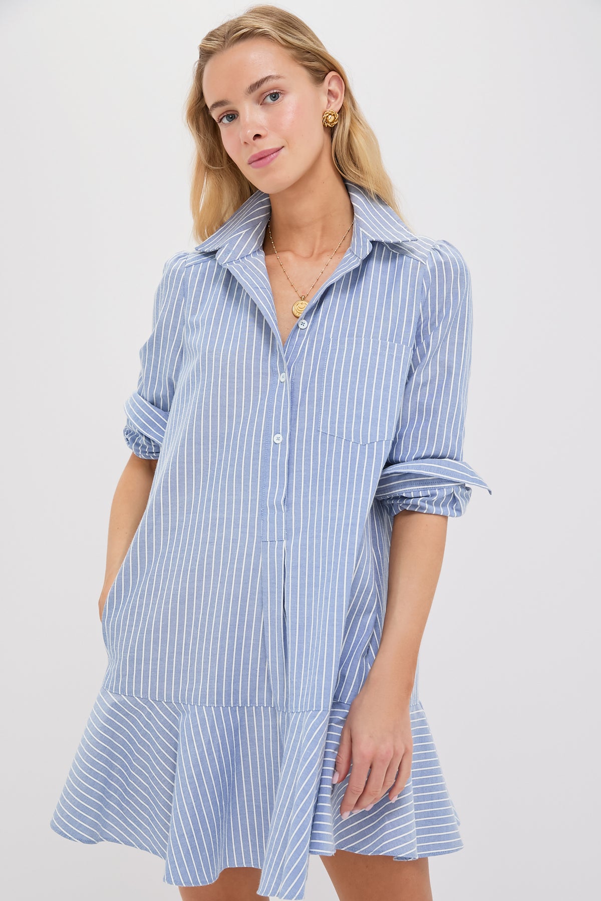 A woman wears the Tuckernuck Callahan Shirt Dress—a blue and white vertically striped button-down with long sleeves, a relaxed swingy fit, and a flutter hemline.