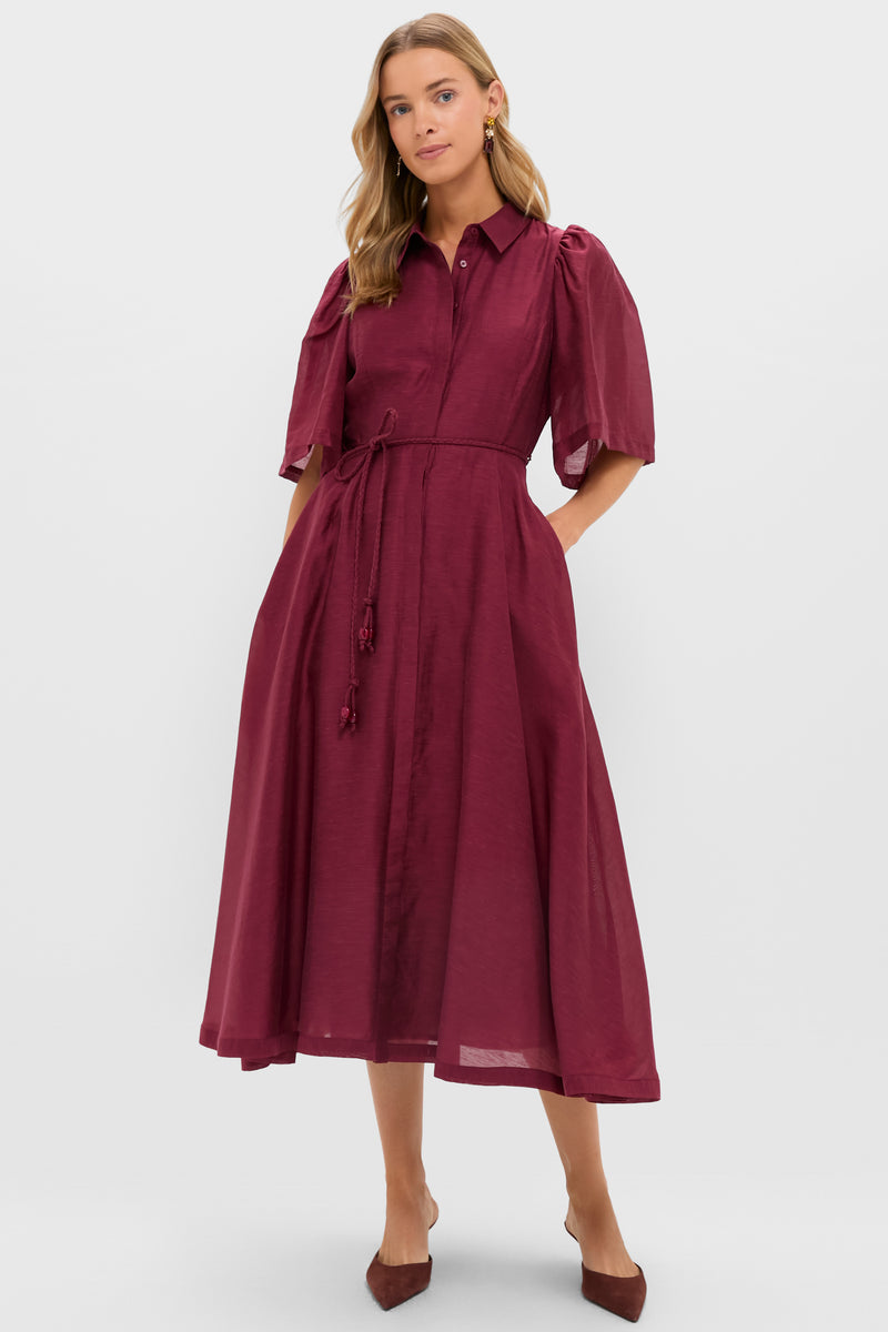 A woman wears the Hyacinth House Cindy Dress in burgundy, featuring puff sleeves, a collared neckline, a tie waist, and paired with brown pointed-toe flats.