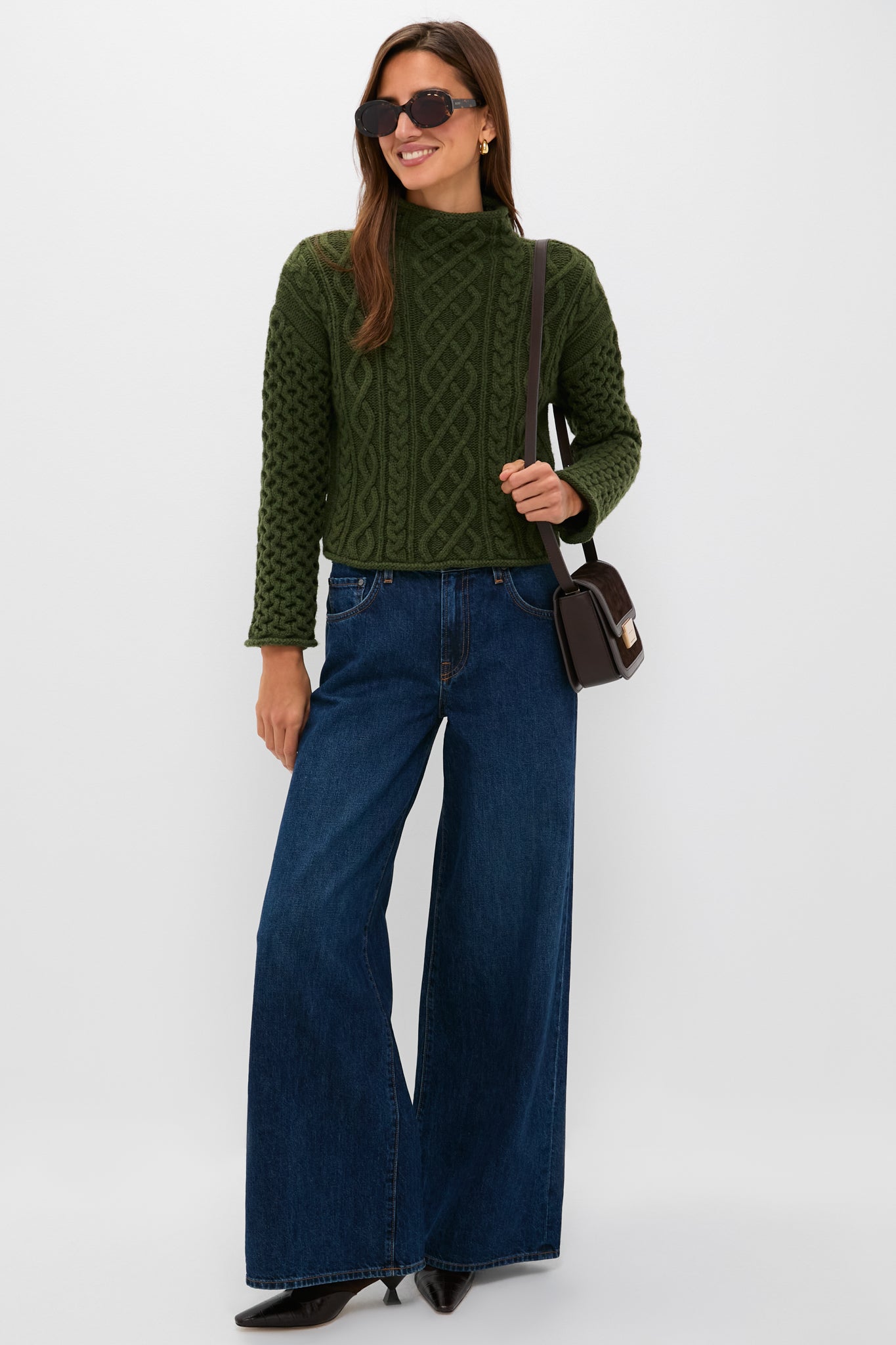 Woman models Olive Cable Knit Cropped Perry Turtleneck, exuding classic, effortless style with dark jeans, black boots, and chic accessories for a high-end, fun look.