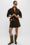 Model in Carob Luz Mini Dress: a classic, high-end, dark brown corduroy shirt-dress with lantern sleeves and flared skirt, styled effortlessly with boots and accessories.