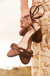 Shea McGee holds brown suede strappy high heel sandals.