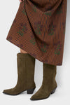 Woman wearing classic Dark Olive Suede Wilson Cowboy Boots with pointed toe and block heel, styled with a floral skirt, embodying effortless, fun, high-end Western charm.