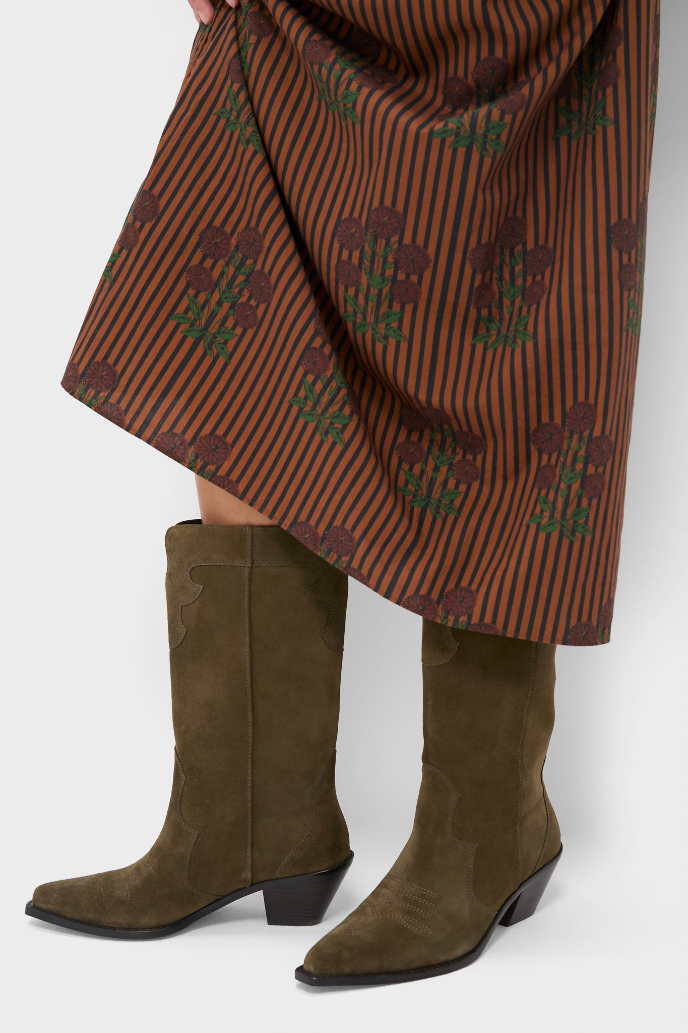 Woman wearing classic Dark Olive Suede Wilson Cowboy Boots with pointed toe and block heel, styled with a floral skirt, embodying effortless, fun, high-end Western charm.