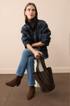 Woman sitting in a blue plaid jacket, brown turtleneck, and jeans. 