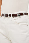 Close-up of Sepia Aiden Studded Rugous Belt in brown leather, featuring a polished silver buckle and studs, paired with cream jeans for a classic, effortless look.
