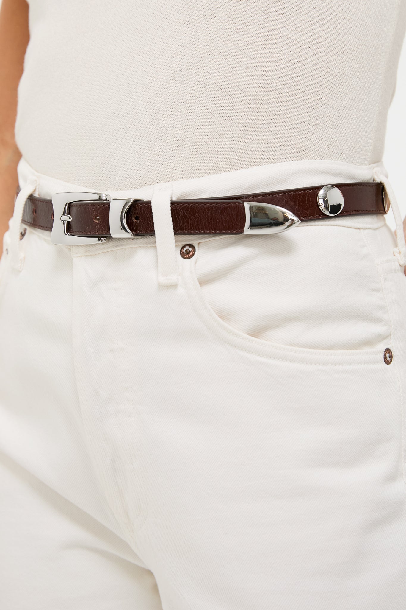 Close-up of Sepia Aiden Studded Rugous Belt in brown leather, featuring a polished silver buckle and studs, paired with cream jeans for a classic, effortless look.