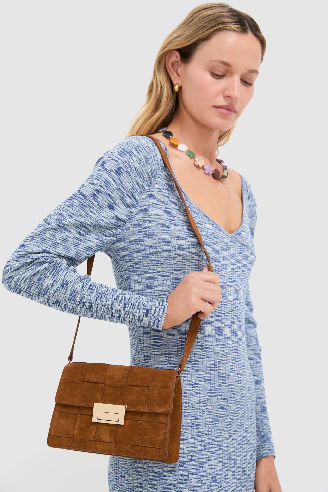 Model with a classic, effortless style showcasing the high-end Woven Cacao Suede Delphine Crossbody Bag, featuring a fun grid-patterned flap and gold clasp.