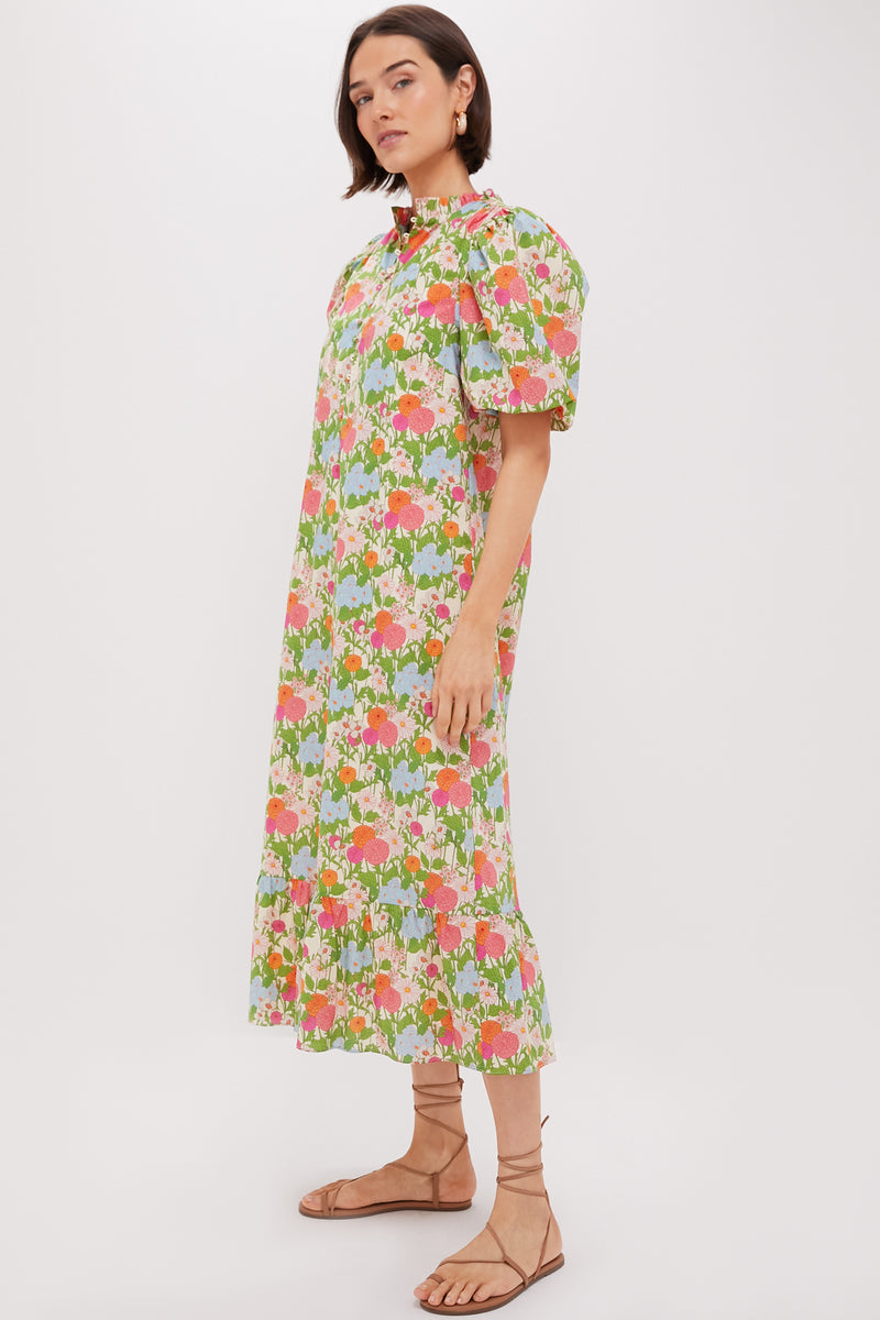 A woman in the Multi Green Begonia Floral Mimi Midi Dress with ruffle collar and puff sleeves, styled with brown strappy sandals—an effortlessly chic boho look.