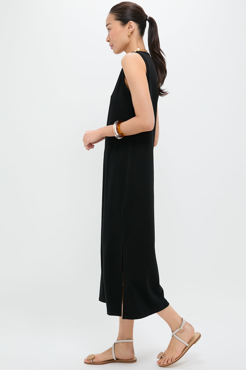 A woman in a Pomander Place sleeveless black cotton-spandex maxi dress with side slits, sandals, and bracelets stands in profile against a plain light background.