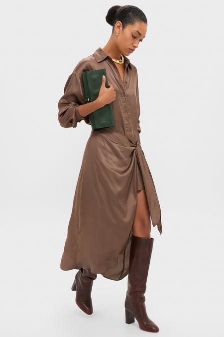 Model wearing the classic Morel Alessandra Sarong Shirt Dress, featuring an effortless twist knot detail and asymmetrical slit, paired with a forest-green clutch and knee-high boots.