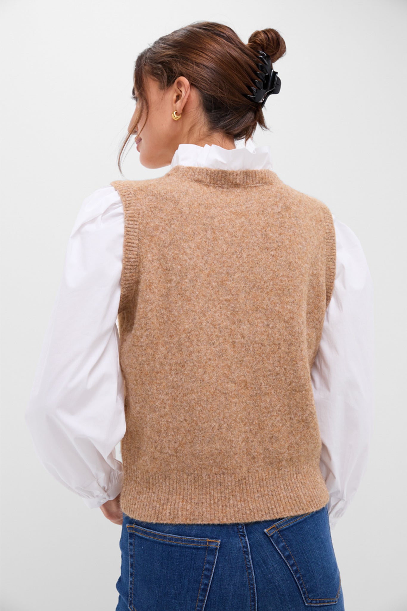 Back view of the Desert Melange Ella Sweater Blouse, showcasing its classic sleeveless vest design over a white puff-sleeve blouse, paired with medium-wash jeans. Effortless, high-end style.