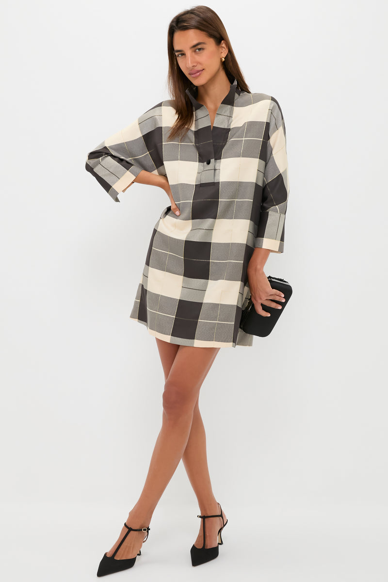A woman poses in a Tuckernuck black and white plaid shift dress with three-quarter sleeves, accessorized with a black clutch and heels, set against a plain white background.