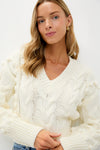Ivory Cable Knit Cropped Contessa V-Neck Sweater, featuring a classic cable-knit design with pom-pom details, effortlessly styled with jeans for a fun, high-end look.