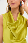 Woman wearing a shiny lime green satin cowl neck top by Tuckernuck and blue statement earrings, shown from shoulders up.