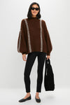 Woman in oversized Brown Mayu Sweater with chic mock neck and embroidered trim, paired with leggings and ballet flats, holding a slouchy black tote. Effortless and high-end style.