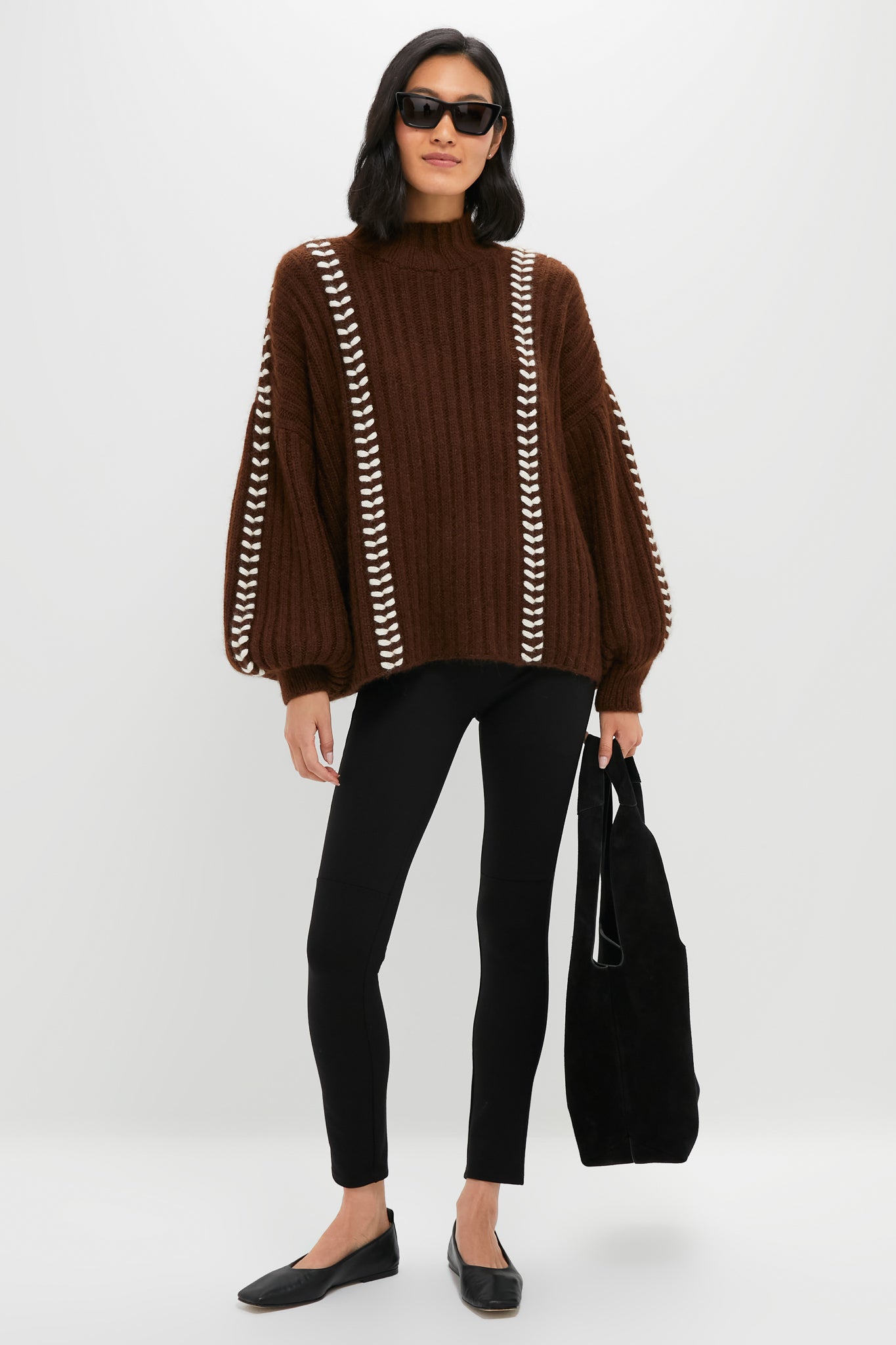 Woman in oversized Brown Mayu Sweater with chic mock neck and embroidered trim, paired with leggings and ballet flats, holding a slouchy black tote. Effortless and high-end style.