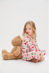 Young girl in Pink Chicken Small Hearts Kids Bamboo Pj Set, lounging against a teddy bear. The classic, effortless pajamas feature a fun, heart-print design, perfect for high-end comfort.