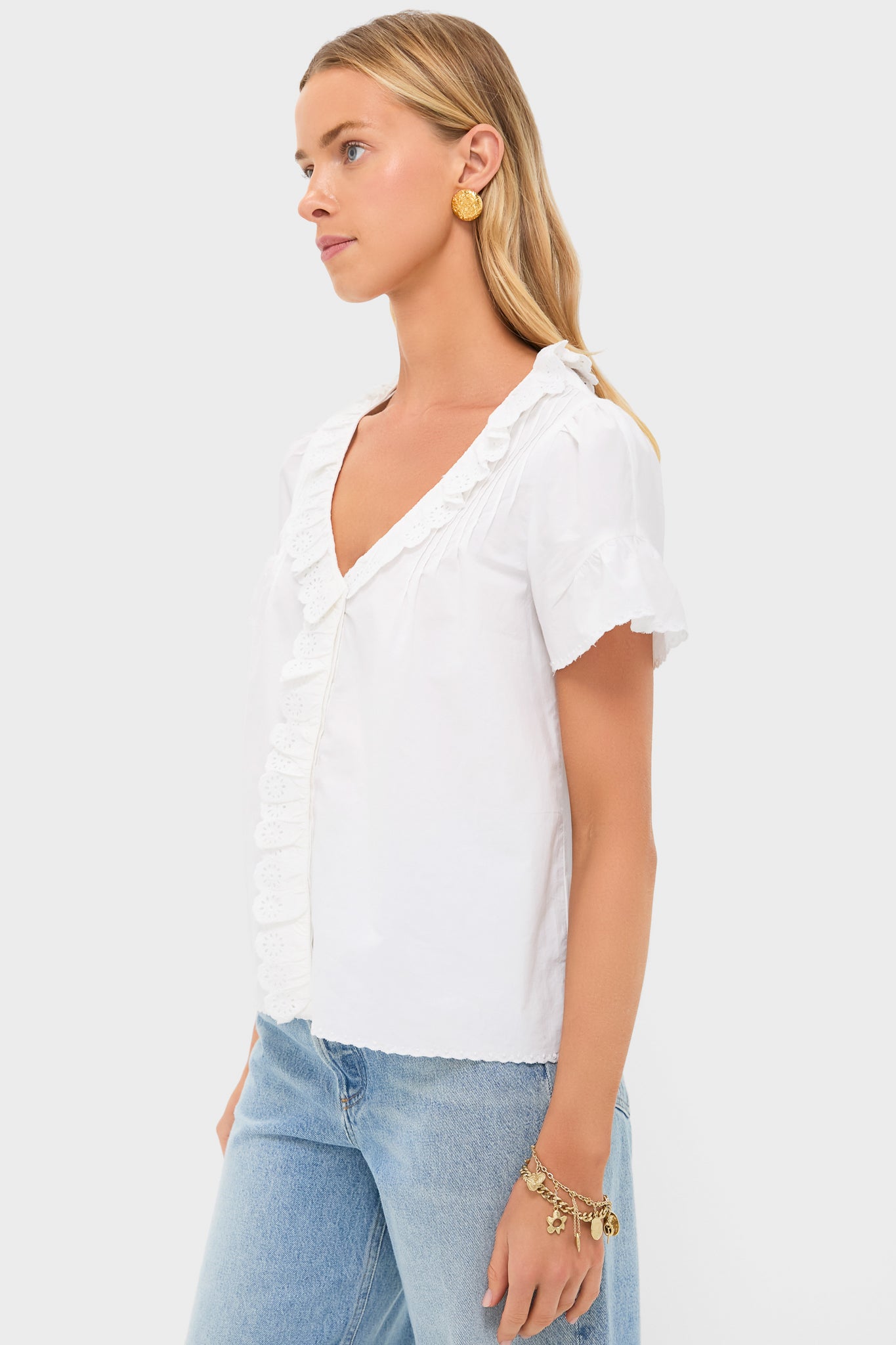 Model wearing the Vintage White Ezra Blouse with eyelet embroidery, scalloped trims, and short flutter sleeves, styled effortlessly with jeans and gold accessories for a classic, high-end look.