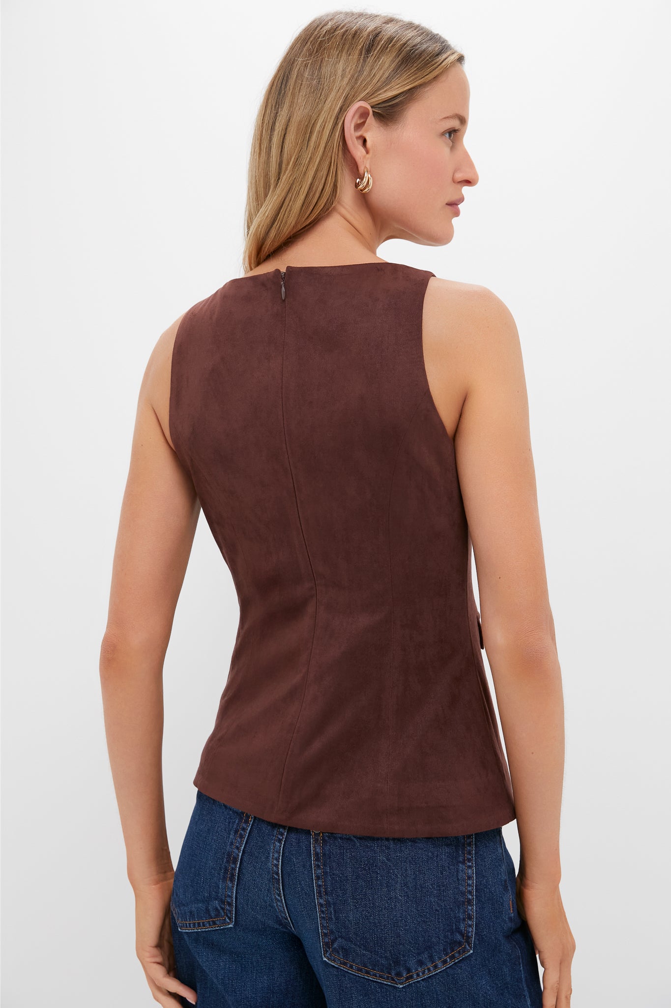 Woman in classic, mocha-brown Brown Faux Suede Franz Top with high neckline, back zip, and gold-accented faux pockets, paired effortlessly with medium-wash jeans.